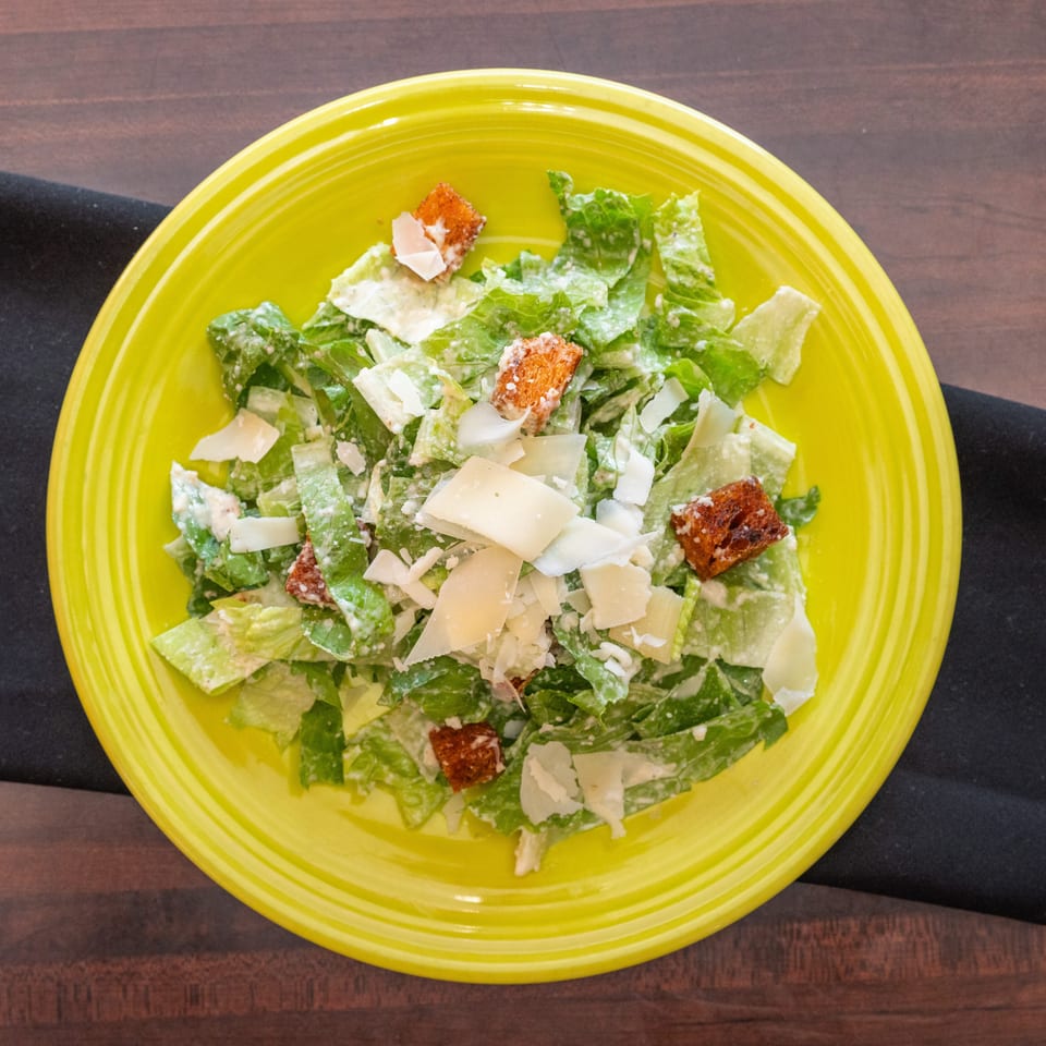 Caesar salad with romaine lettuce, croutons, and parmesan cheese on a bright yellow plate.