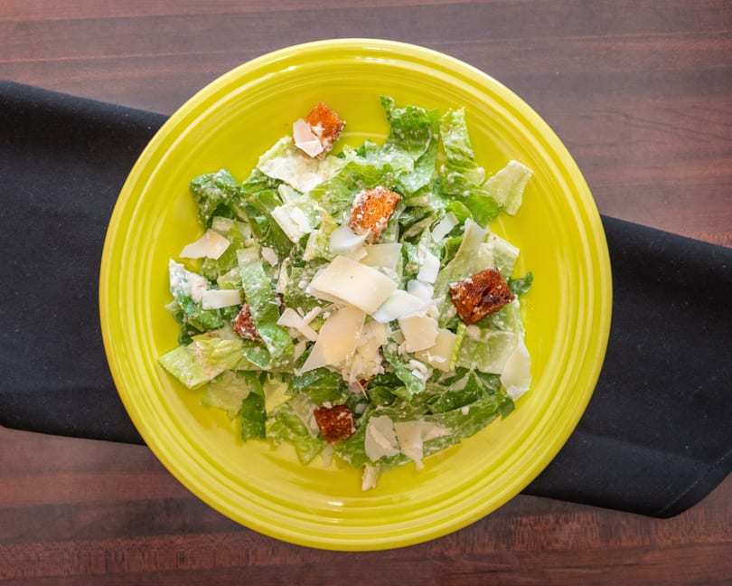 Caesar salad with romaine lettuce, croutons, and parmesan cheese on a bright yellow plate.