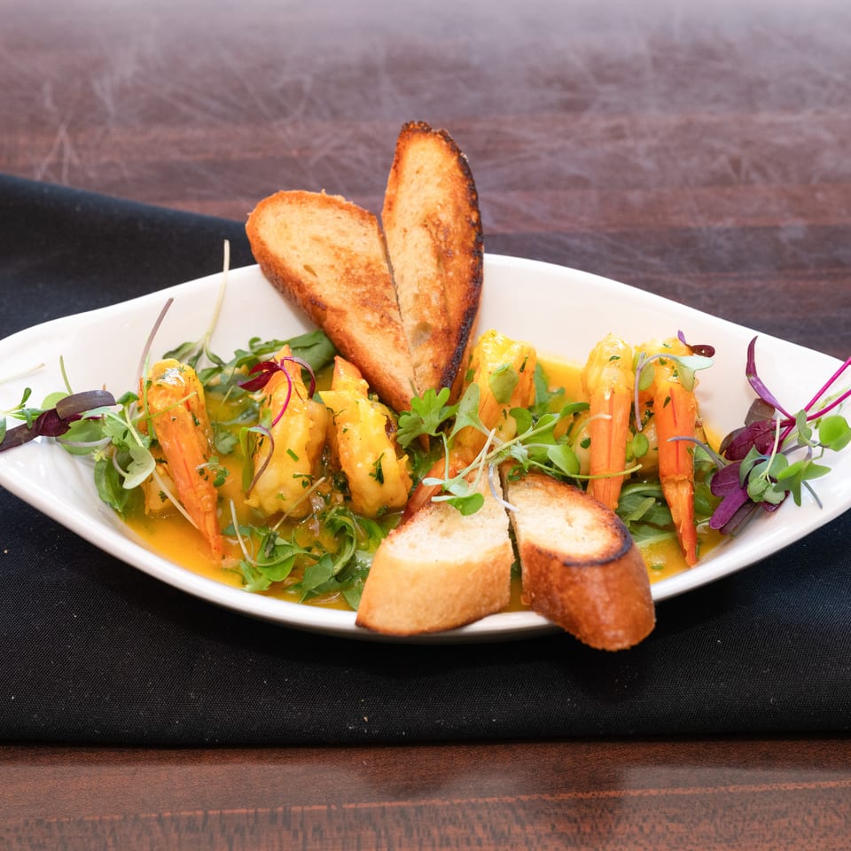 Shrimp scampi in a white bowl with toasted bread, garnished with fresh herbs.