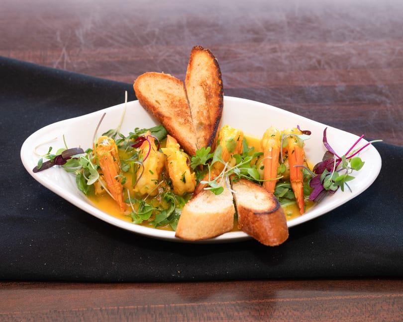 Shrimp scampi in a white bowl with toasted bread, garnished with fresh herbs.