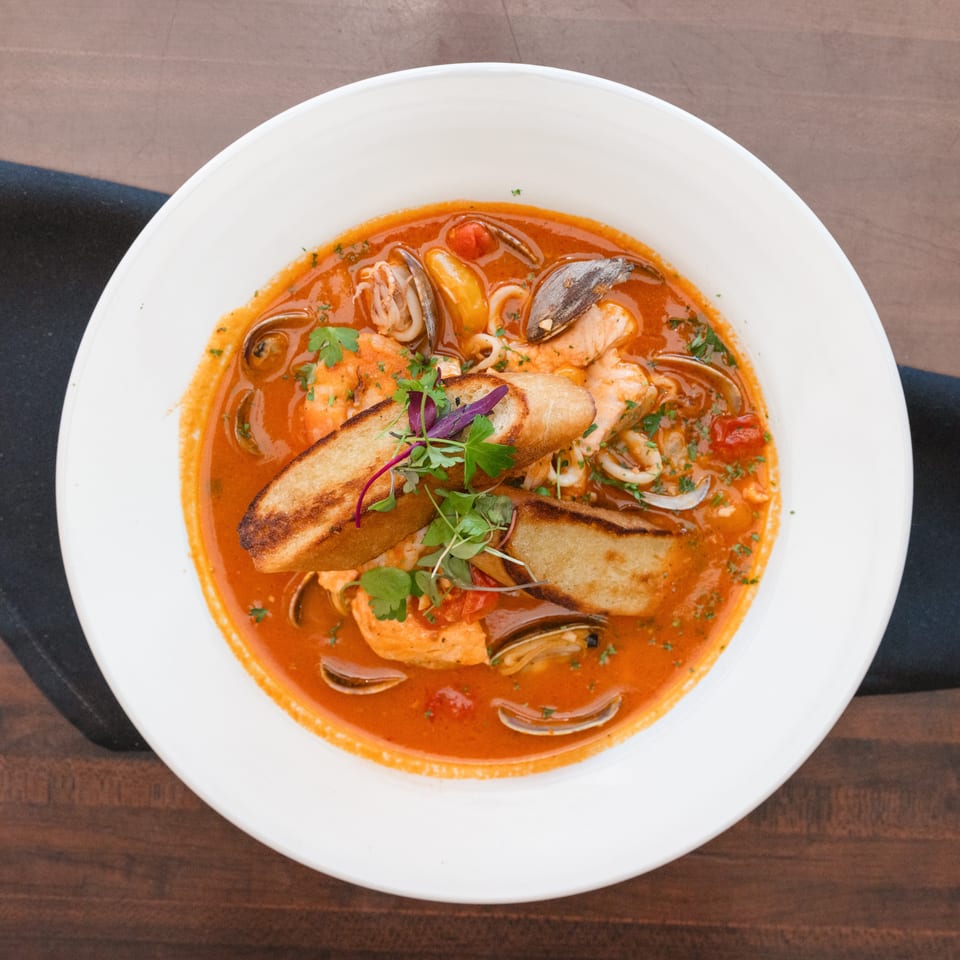 Seafood cioppino with shrimp, clams, mussels, and fish in a rich tomato broth, garnished with bread.