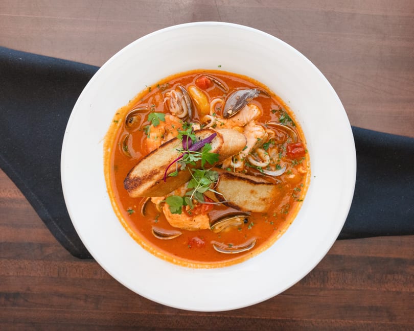 Seafood cioppino with shrimp, clams, mussels, and fish in a rich tomato broth, garnished with bread.