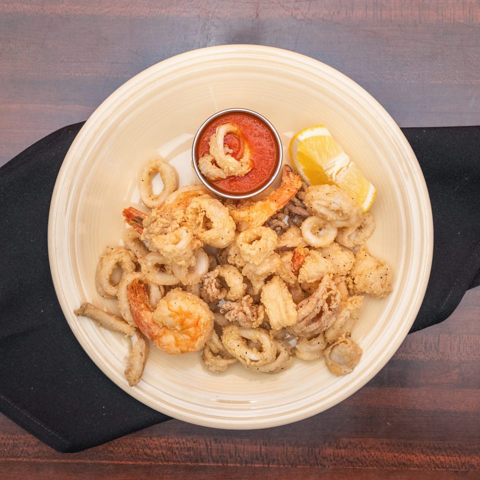 Fried calamari and shrimp with marinara sauce and a lemon wedge on a light yellow plate.