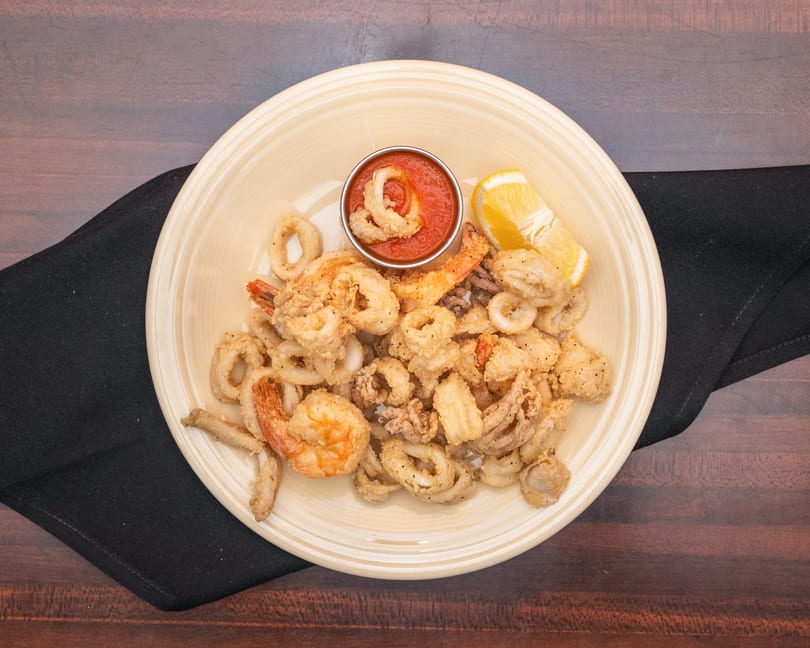 Fried calamari and shrimp with marinara sauce and a lemon wedge on a light yellow plate.