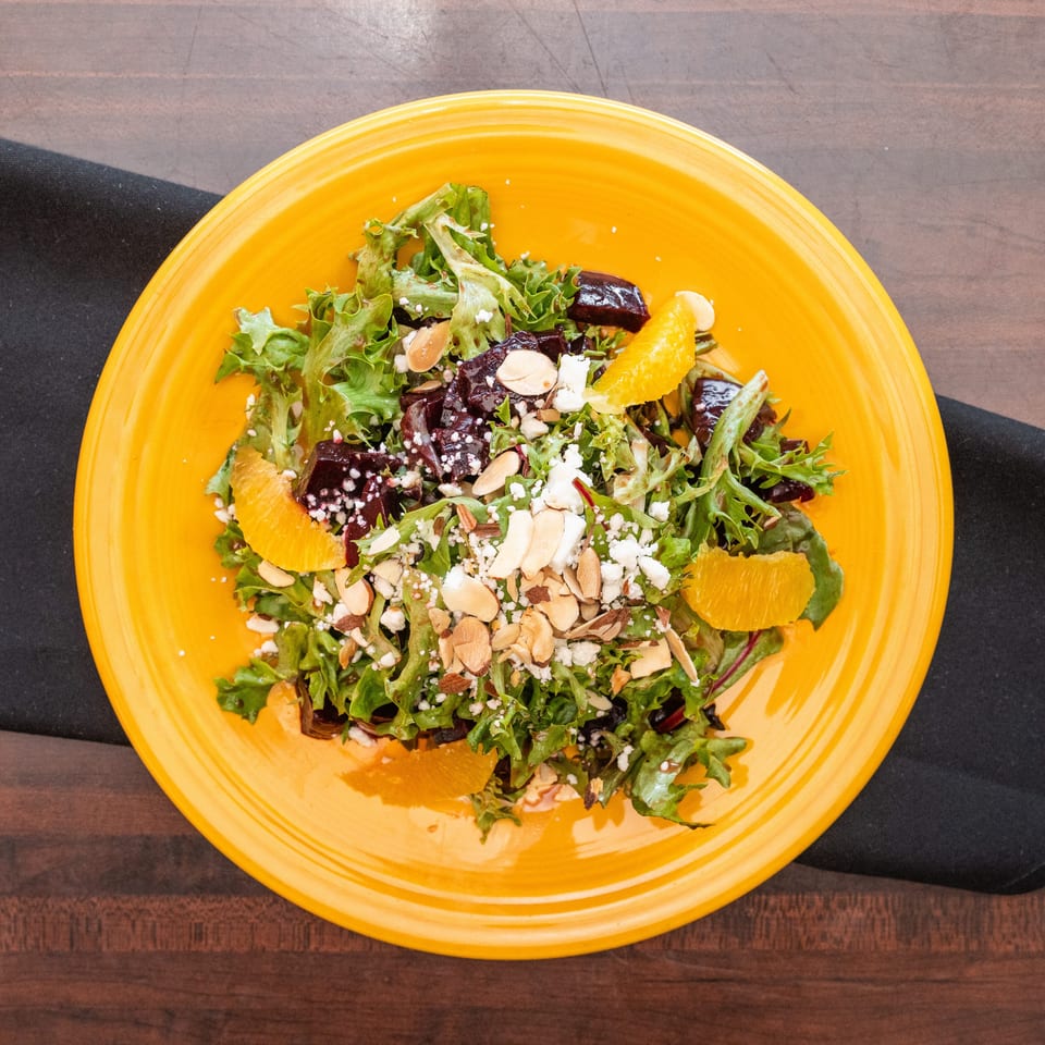Vibrant salad with mixed greens, roasted beets, orange segments, feta cheese, and sliced almonds.