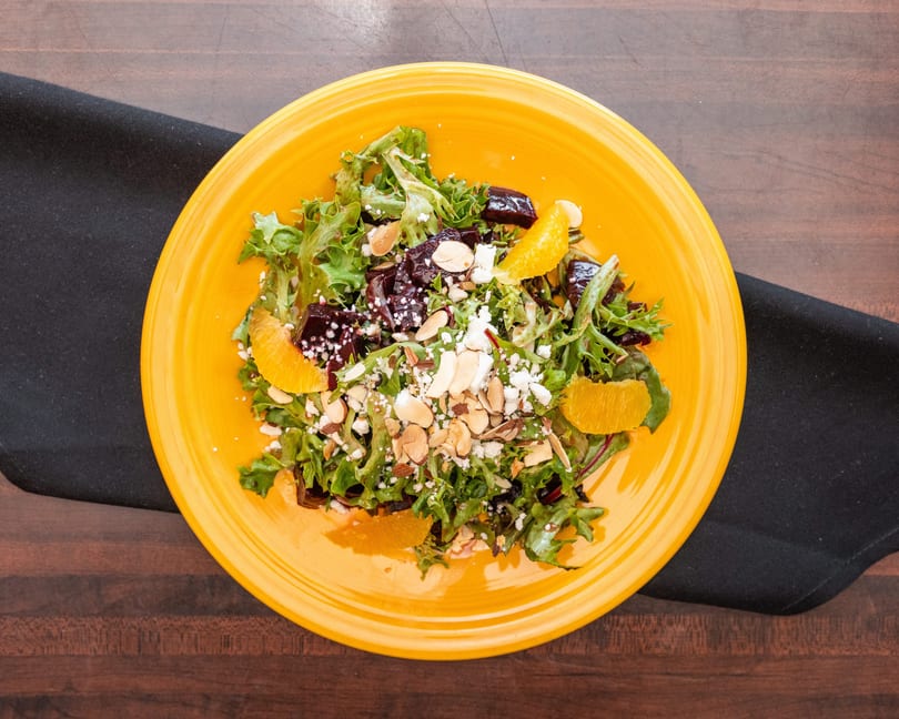 Vibrant salad with mixed greens, roasted beets, orange segments, feta cheese, and sliced almonds.