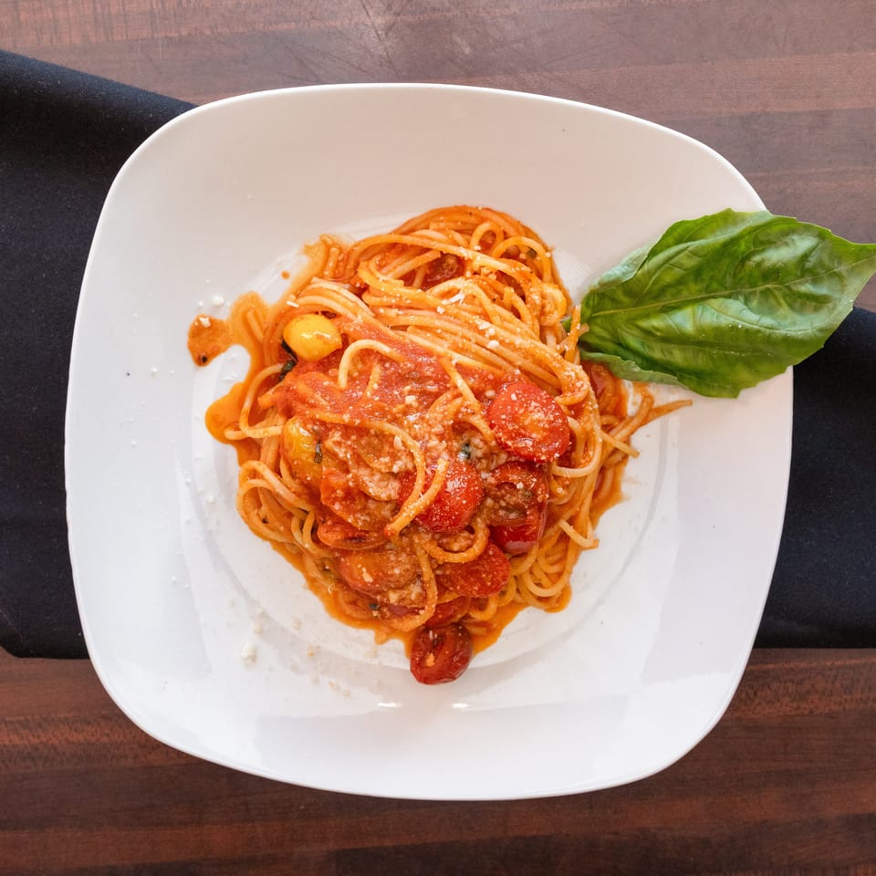 Spaghetti with tomato sauce, cherry tomatoes, Parmesan cheese, and a basil leaf on a white plate.
