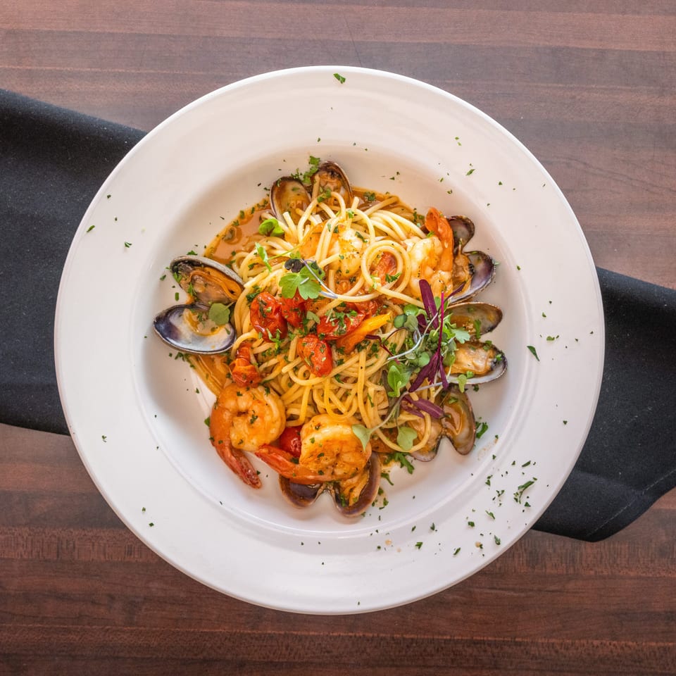 Seafood pasta with shrimp, clams, mussels, cherry tomatoes, and herbs in a white bowl.