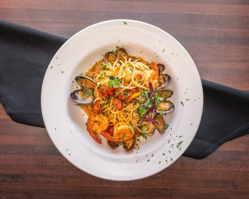 Seafood pasta with shrimp, clams, mussels, cherry tomatoes, and herbs in a white bowl.