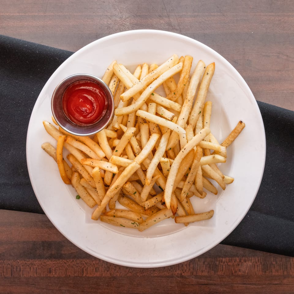 A white plate filled with golden french fries and a side of ketchup on a dark wooden table.