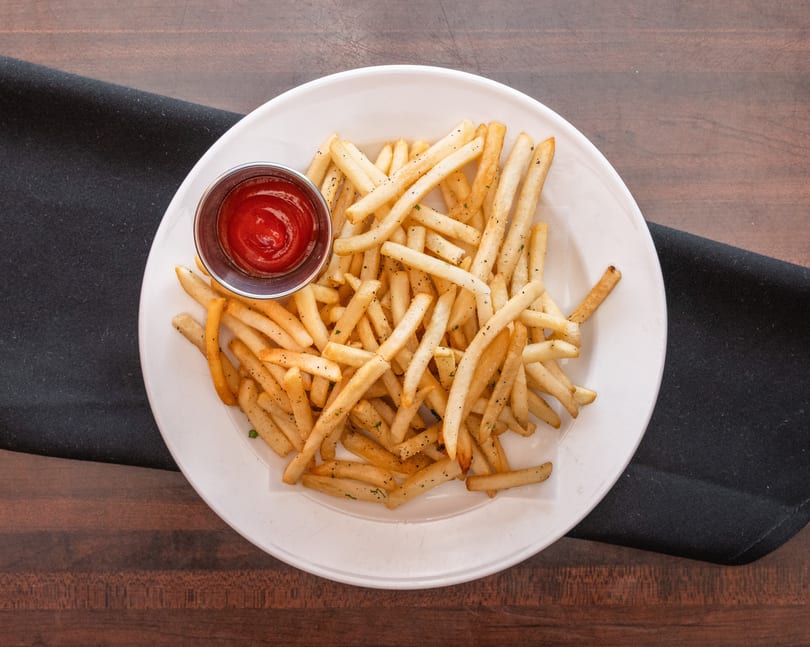 A white plate filled with golden french fries and a side of ketchup on a dark wooden table.