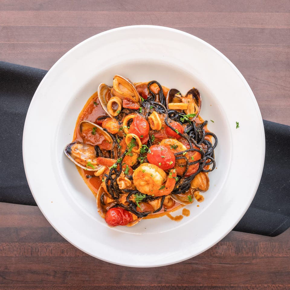 Black squid ink pasta with shrimp, clams, squid, and cherry tomatoes in a red sauce.