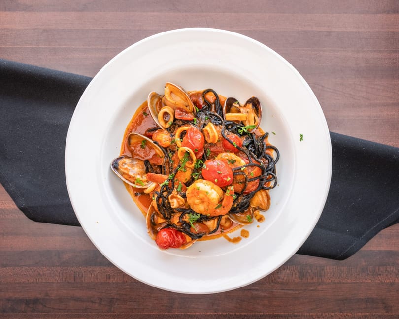 Black squid ink pasta with shrimp, clams, squid, and cherry tomatoes in a red sauce.
