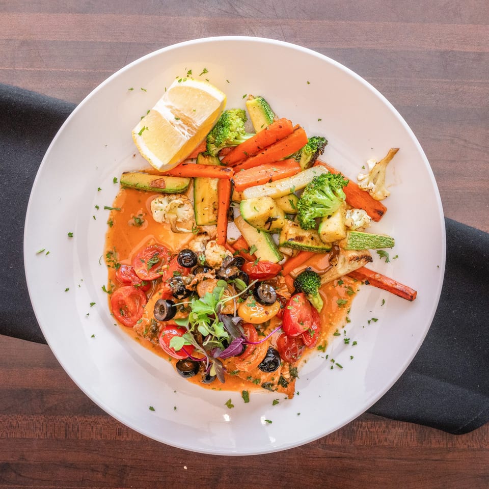 Grilled salmon with roasted vegetables, cherry tomatoes, olives, and a lemon wedge.